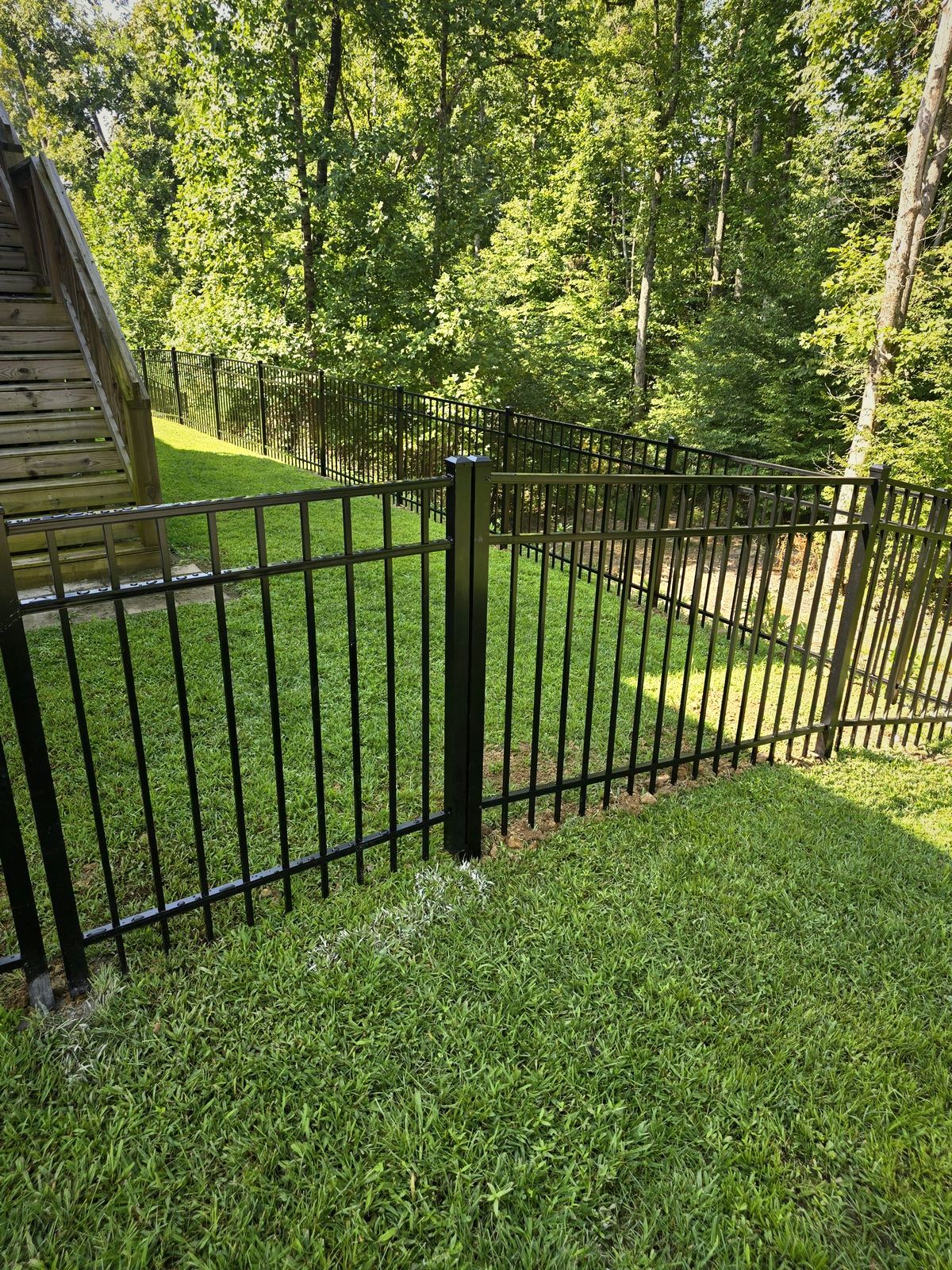Black aluminum fence beside exterior stairs in a wooded yard