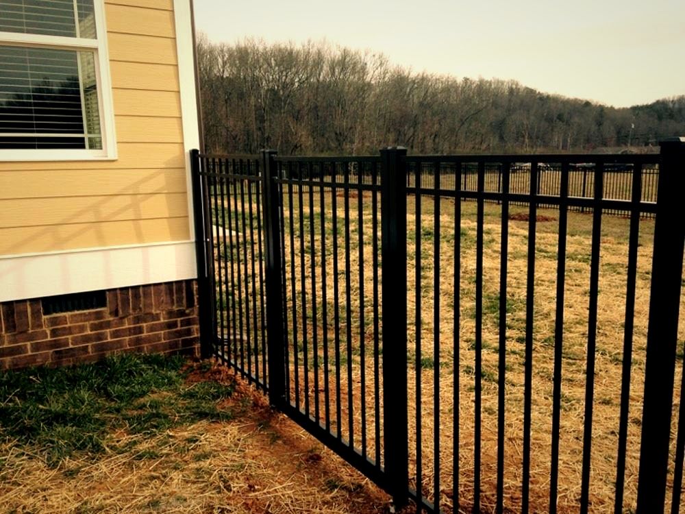 Black aluminum fence meeting the corner of a yellow-sided home
