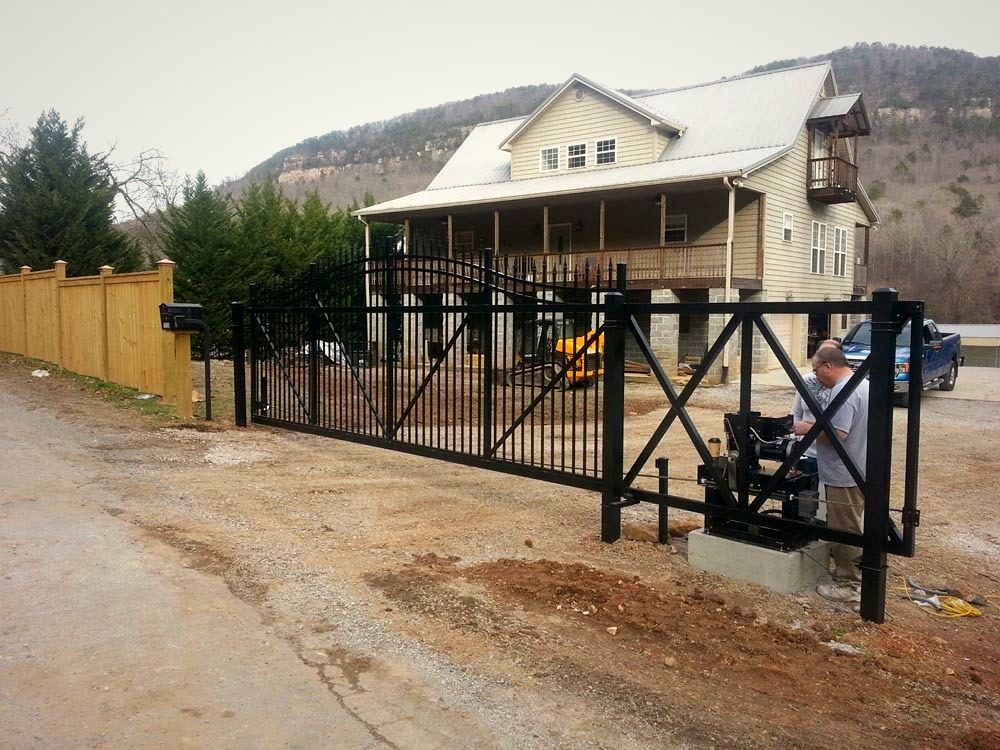 Black aluminum driveway gate in front of a mountain home