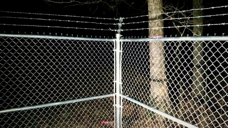 Chain link fence corner topped with barbed wire at night