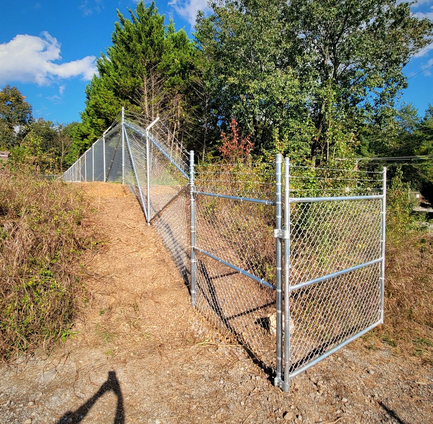 Galvanized chain link fence and gate on a wooded slope