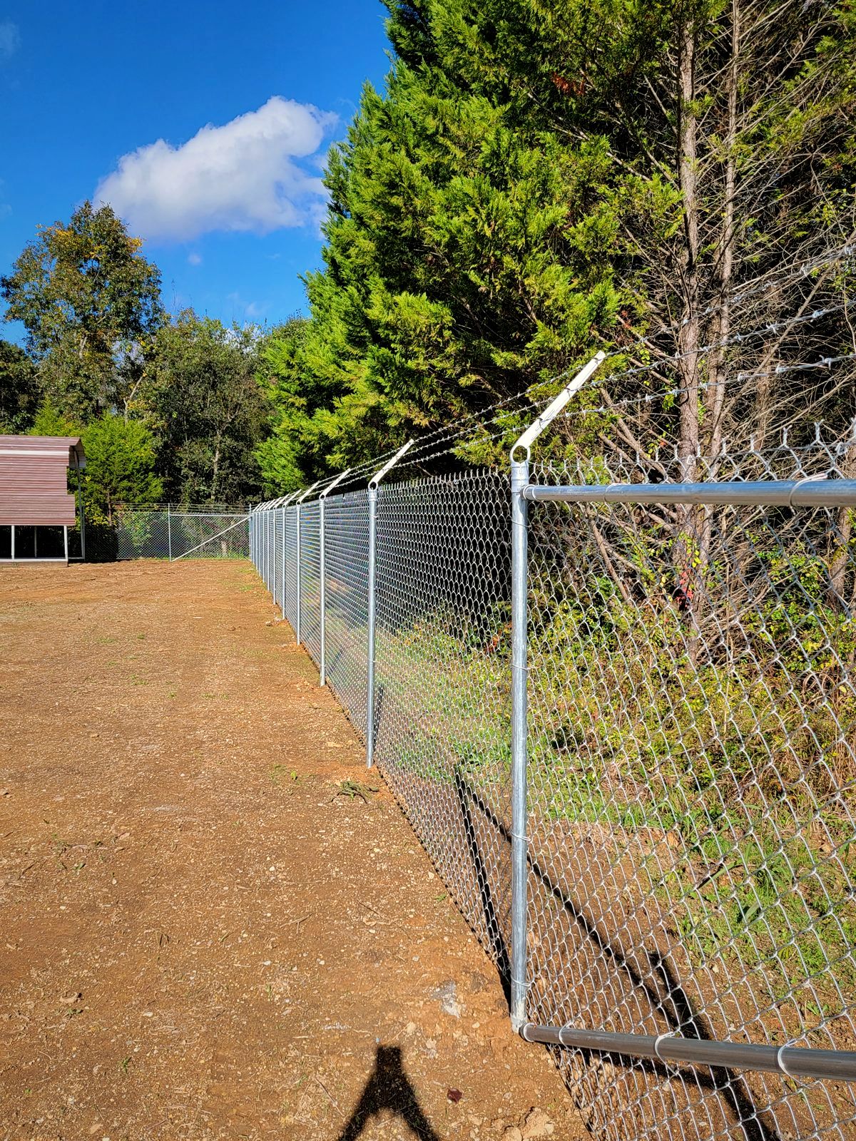 Galvanized chain link fence with barbed-wire arms along a cleared lot