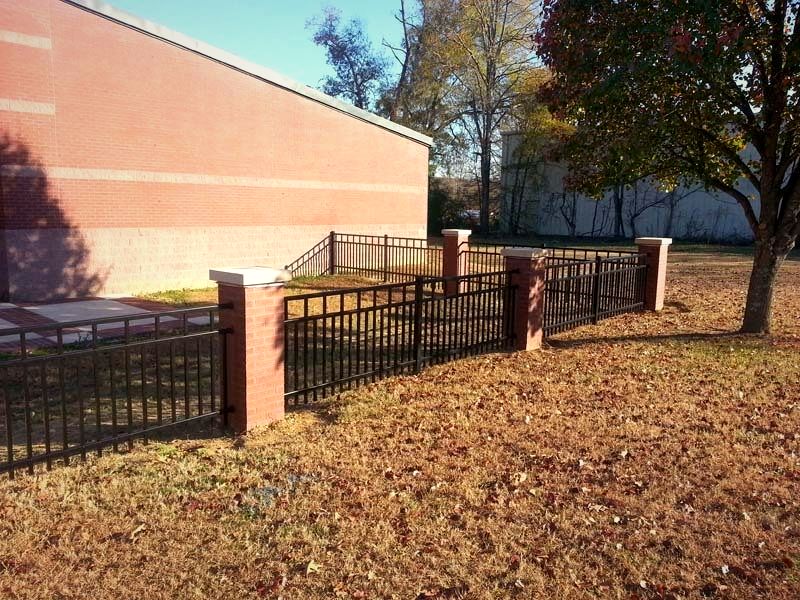 Black aluminum fence with brick piers beside a commercial building