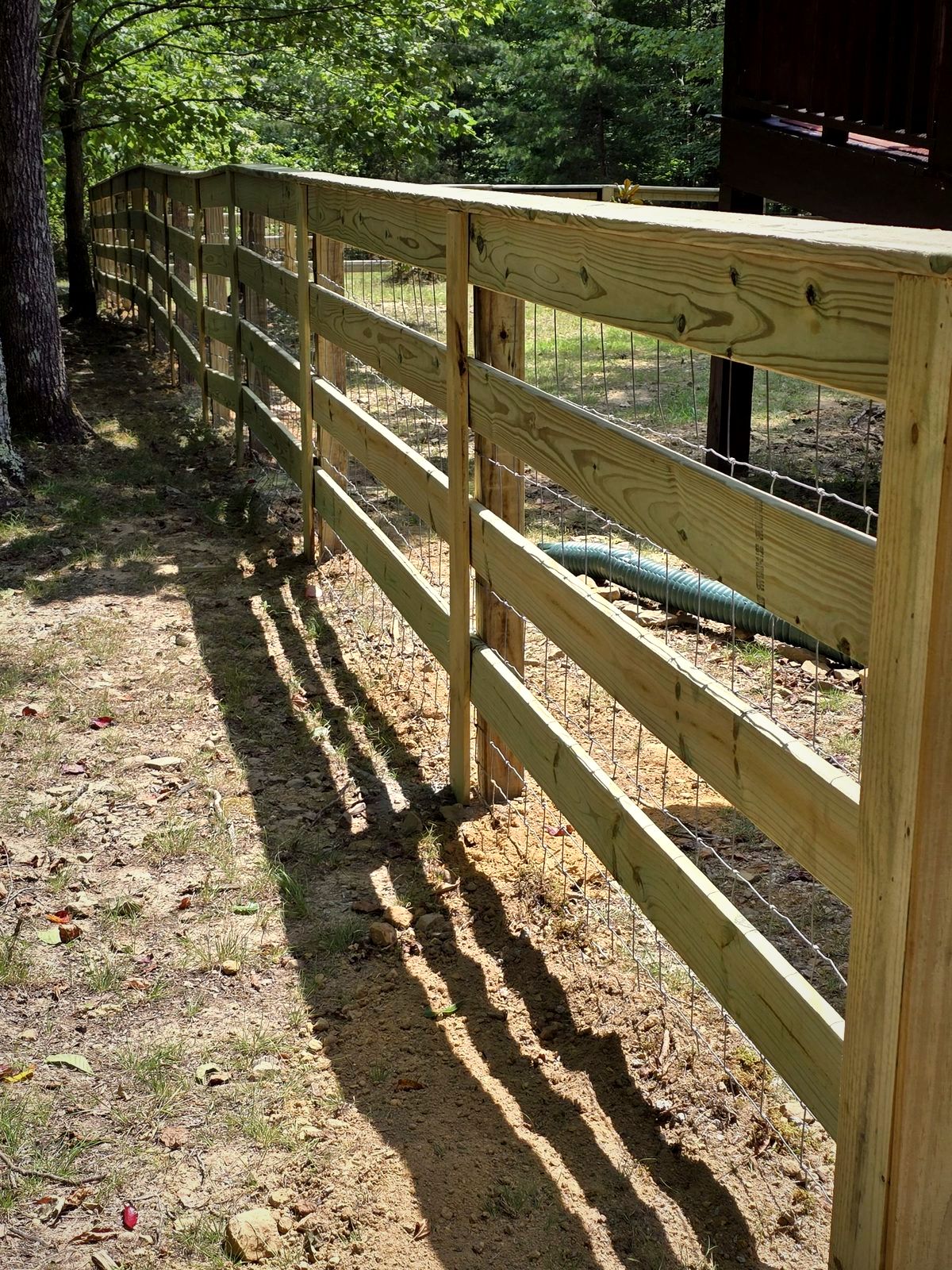 Four-board wood fence with wire mesh in a wooded lot