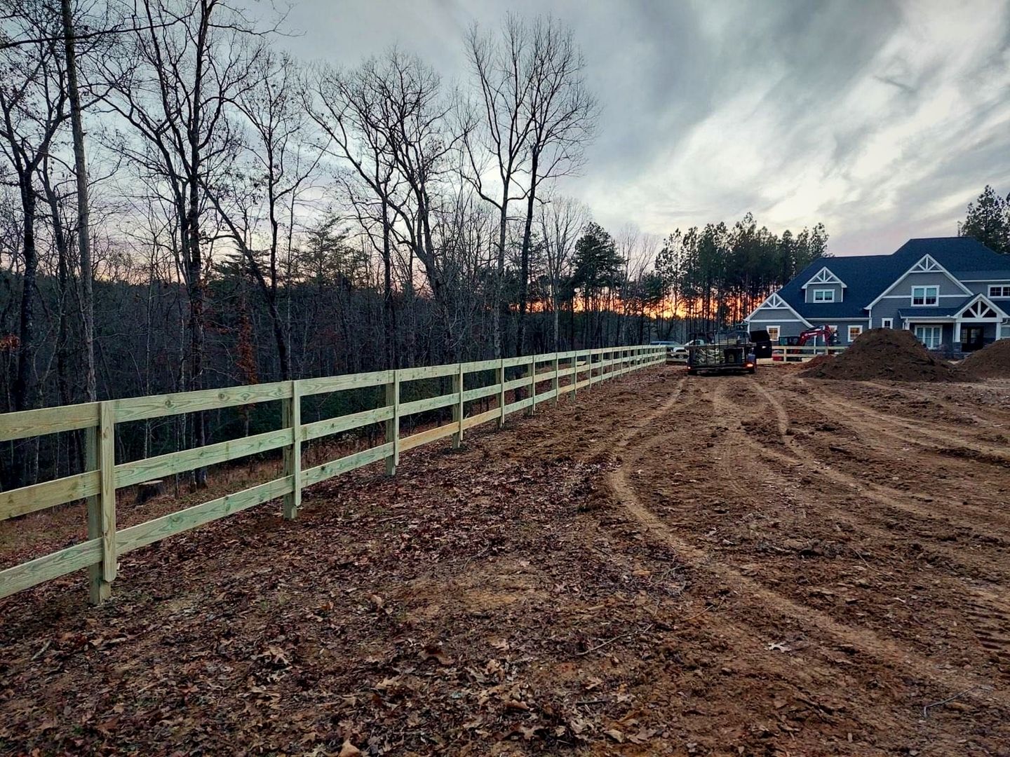 Three-rail wood fence across a freshly graded field at dusk