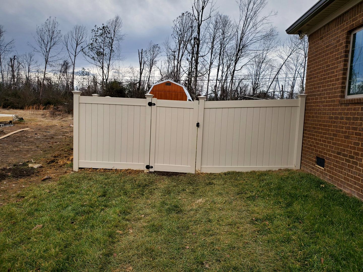 Tan vinyl privacy fence with a double gate beside a brick home