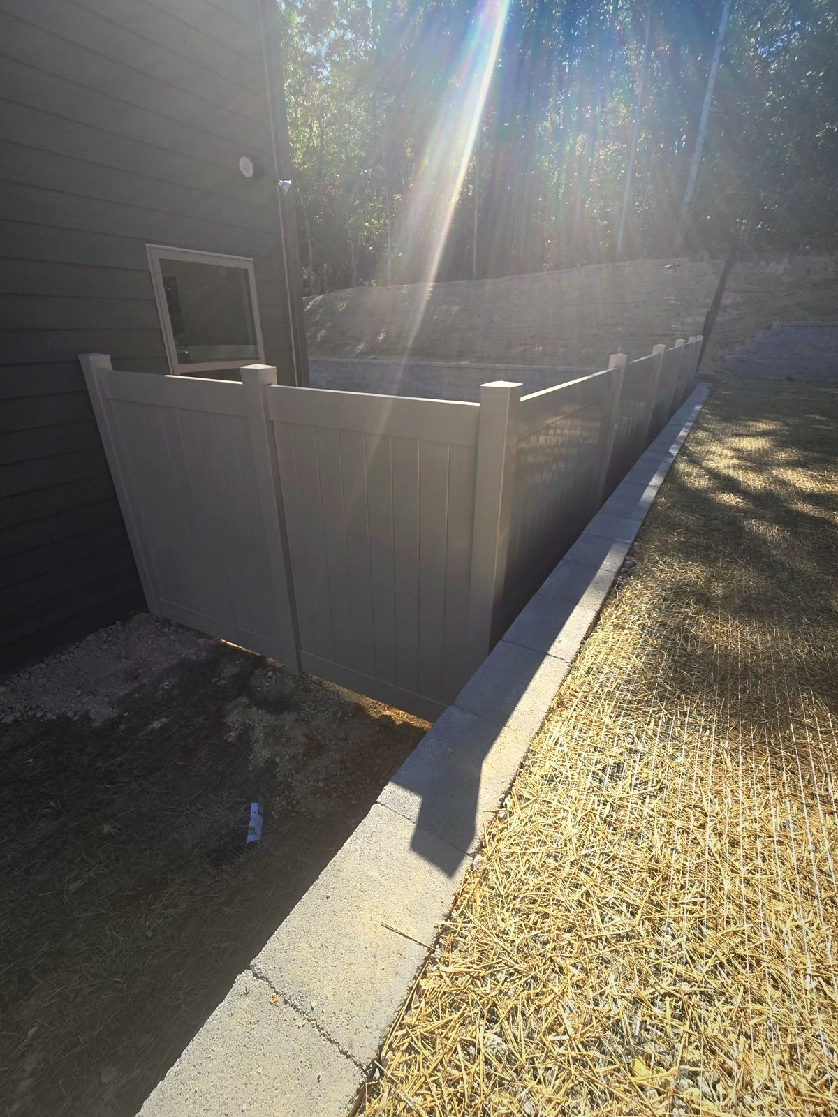 Gray vinyl privacy fence along a gravel side yard