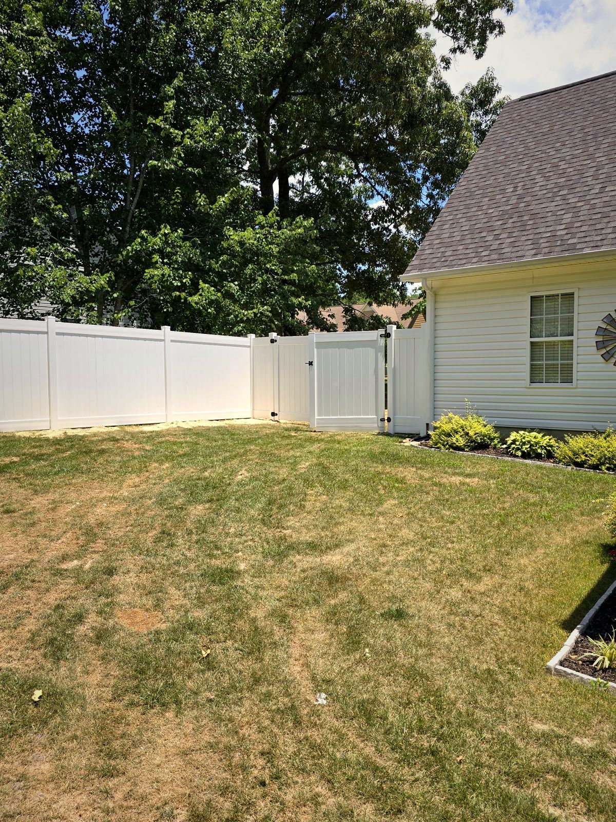 White vinyl privacy fence with a walk gate beside a home