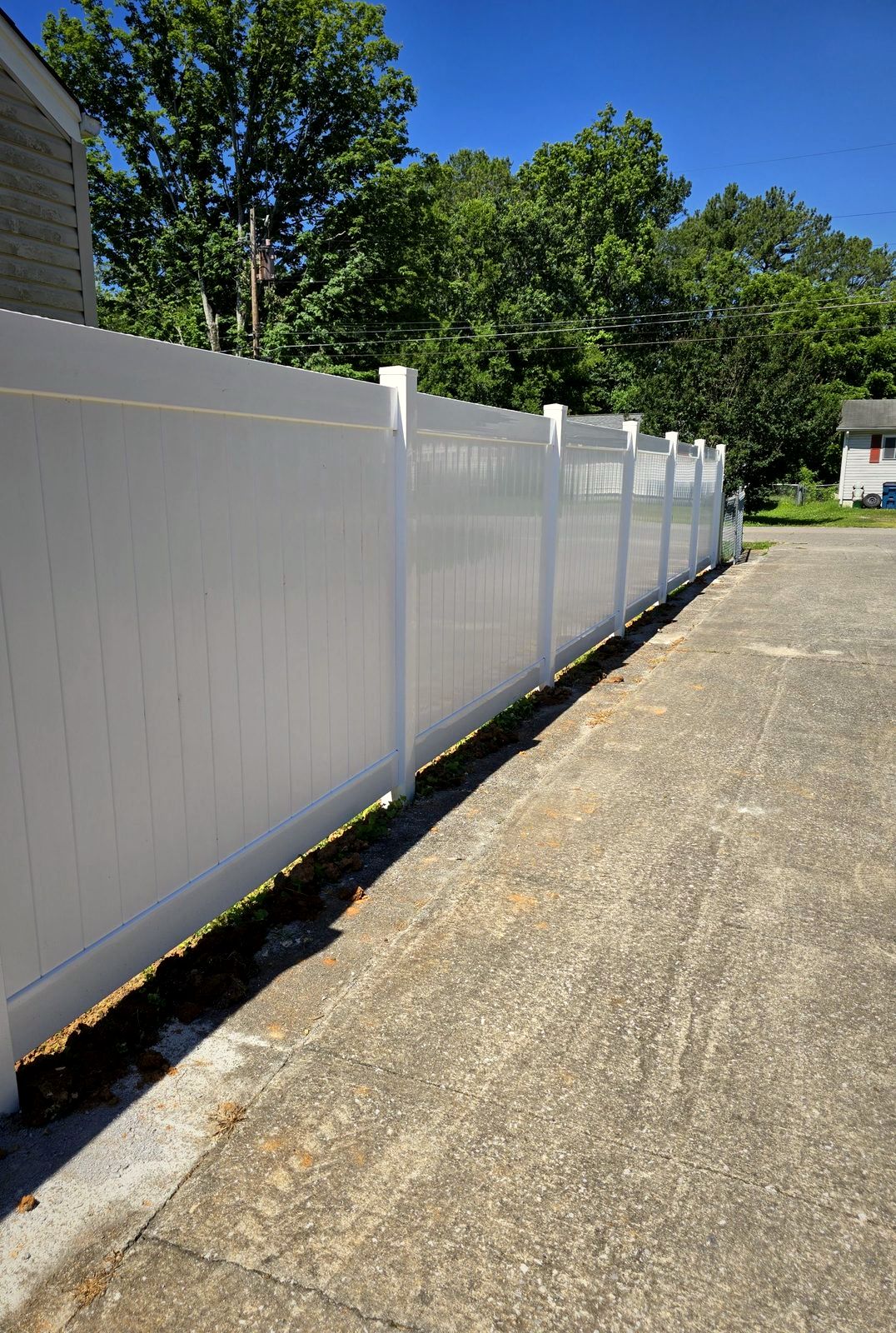 White vinyl privacy fence along a concrete driveway
