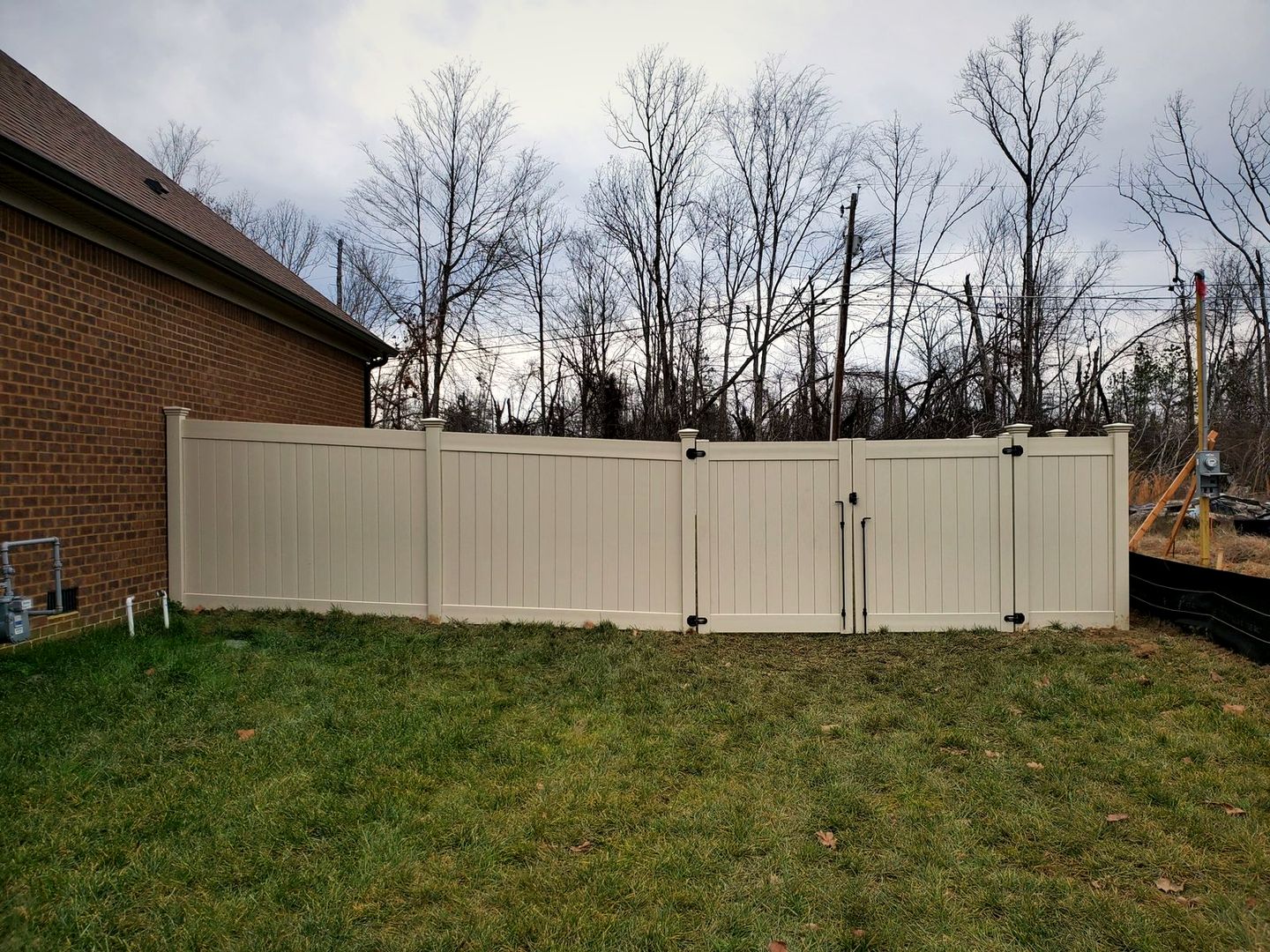 Tan vinyl privacy fence with a double gate behind a brick home