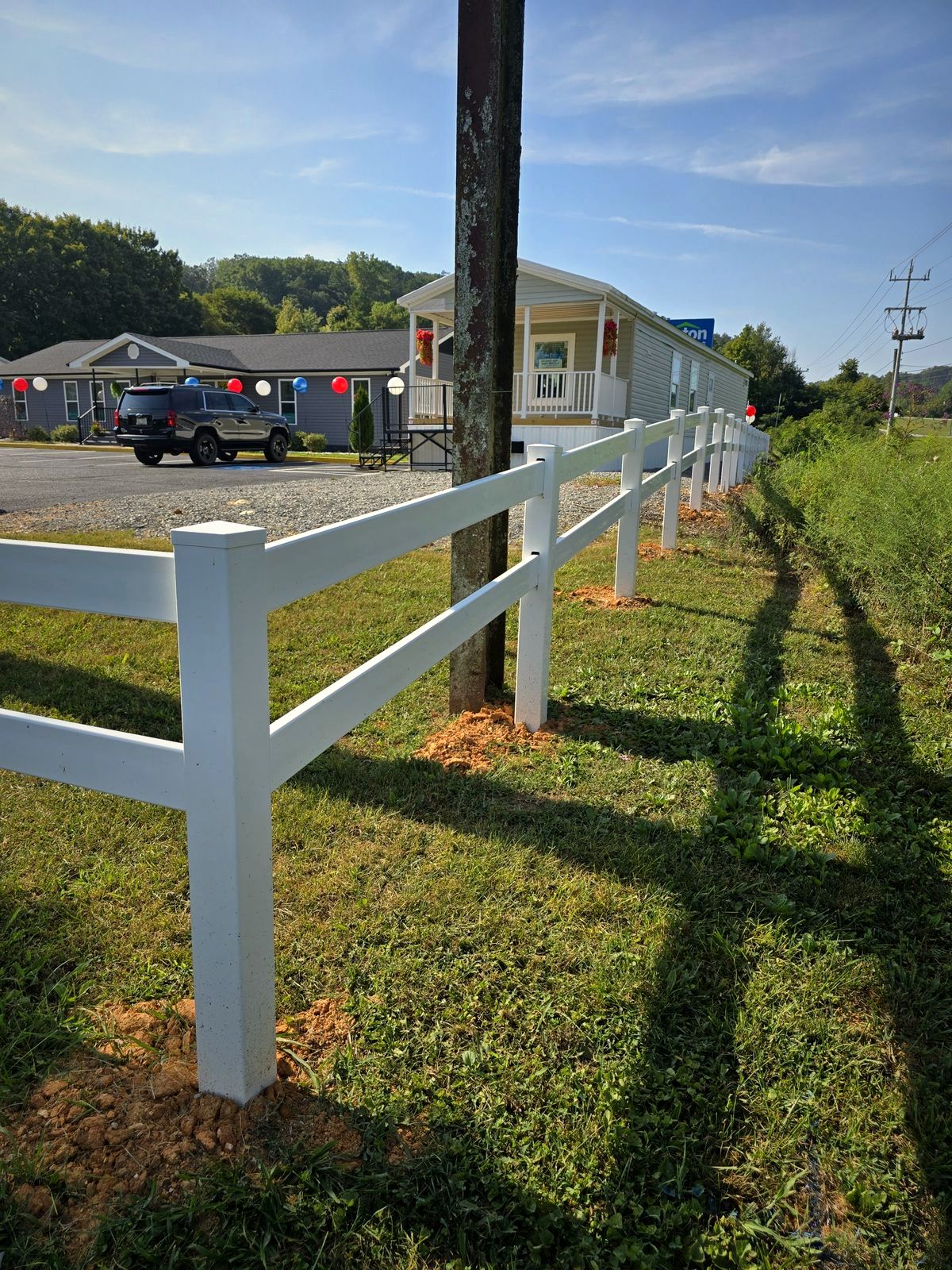 White vinyl two-rail fence along a roadside lawn