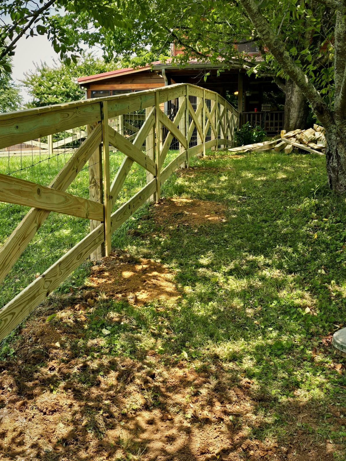 Wood crossbuck rail fence with wire mesh along a shaded yard