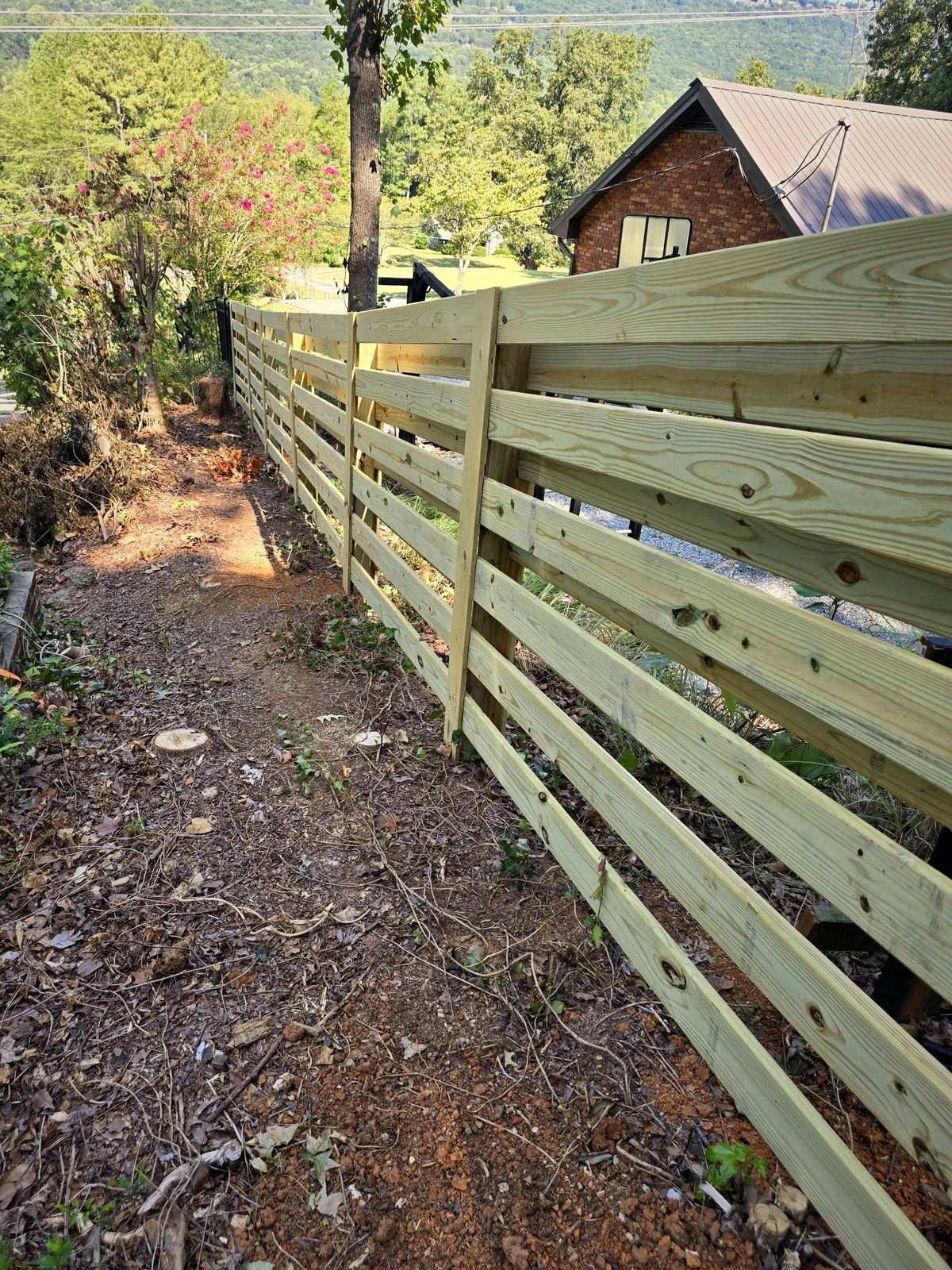 Horizontal board wood fence beside a brick home with hills behind