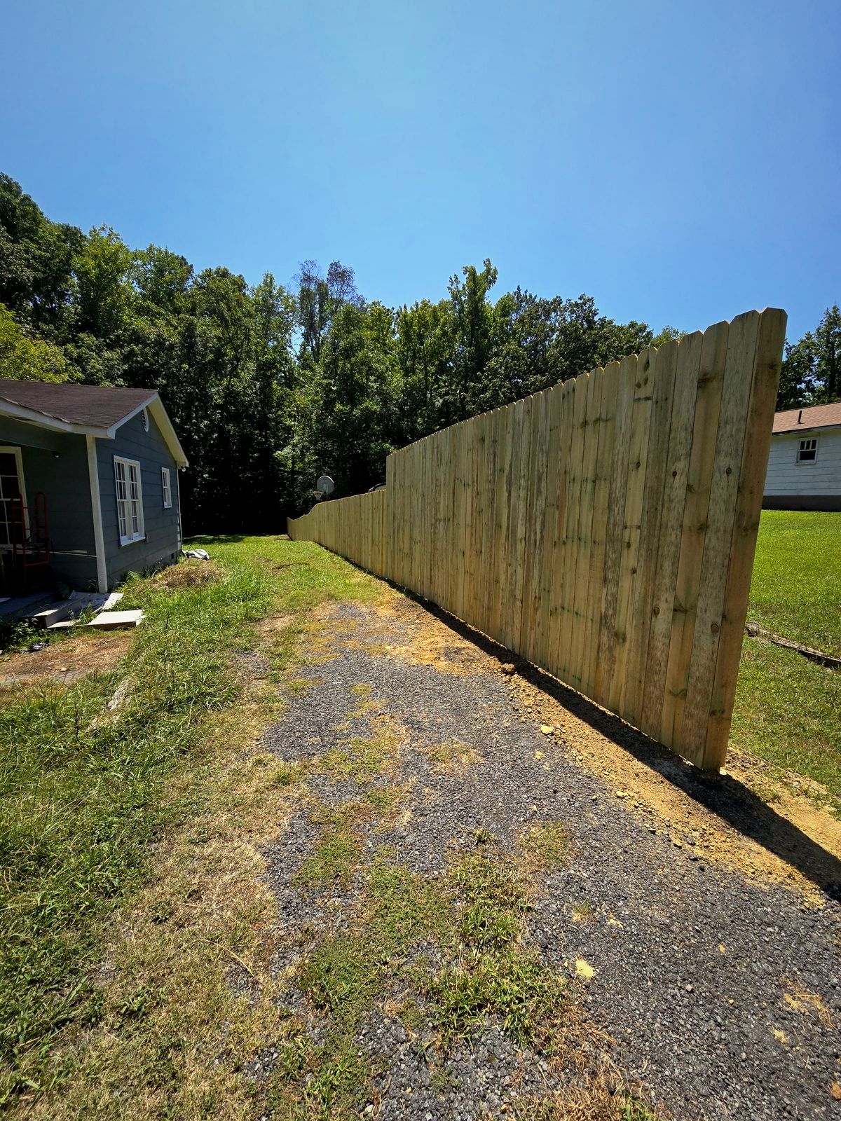 Tall wood privacy fence along a gravel drive